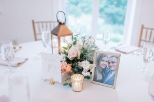 Beautiful wedding centerpiece with copper lantern, table number, a small floral arrangement and a framed photo of the bride and groom.